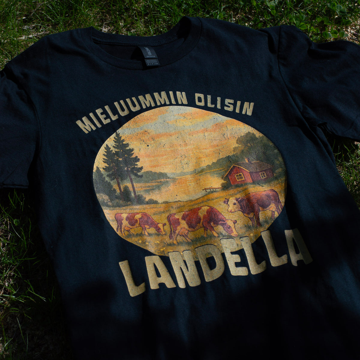 Musta Mieluummin olisin landella -miesten t-paita maalaismaisemaprintillä, aseteltuna sammalelle.