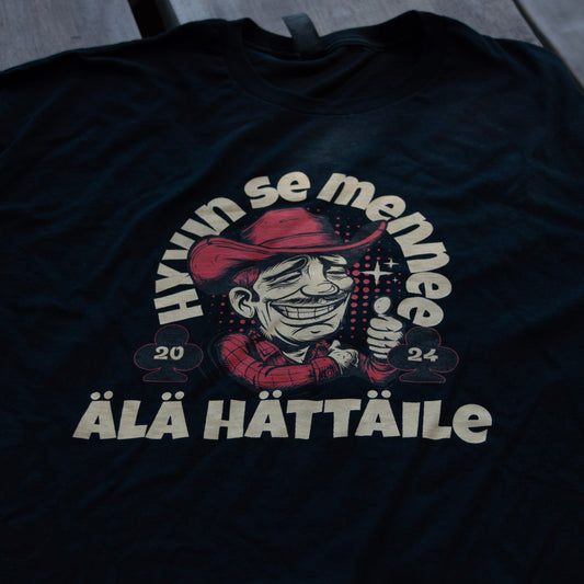 Musta Hyvin se mennee -t-paita, jossa cowboy-kuvitus ja teksti Älä hättäile, aseteltuna tasaiselle alustalle.
