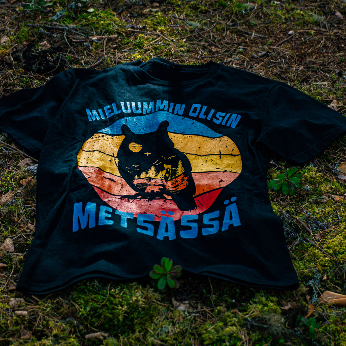 Musta Mieluummin olisin metsässä -t-paita pöllöprintillä, aseteltuna metsämaahan.
